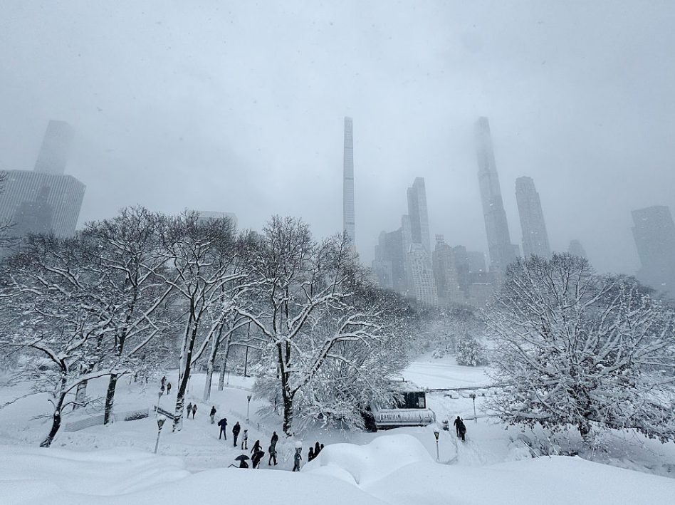 सेंट्रल पार्क में बर्फबारी के दौरान लोग चलते, skyscrapers पीछे – iconic NYC winter scene। new york flights cancelled