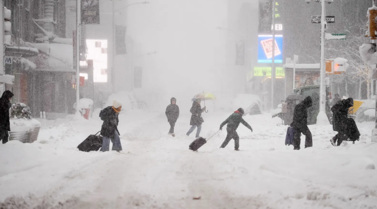 न्यूयॉर्क की व्यस्त सड़कें बर्फ से ढकी, लोग सामान लेकर चलते – travel chaos का जीवंत उदाहरण।new york flights cancelled