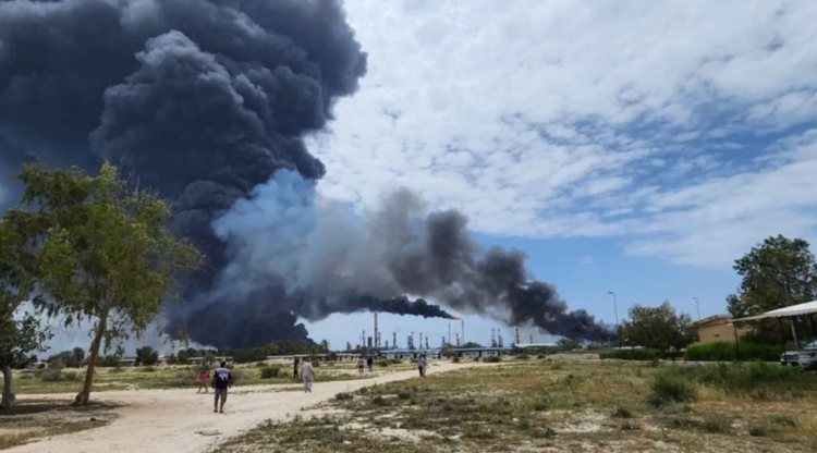 लवान द्वीप पर ईरान ऑयल रिफाइनरी हमले के बाद दूर से दिखता काला धुआं और लोग देखते हुए | iran oil refinery